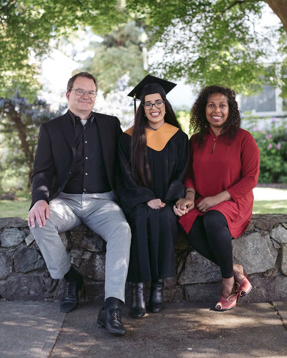 graduate and parents sitting on stone wall